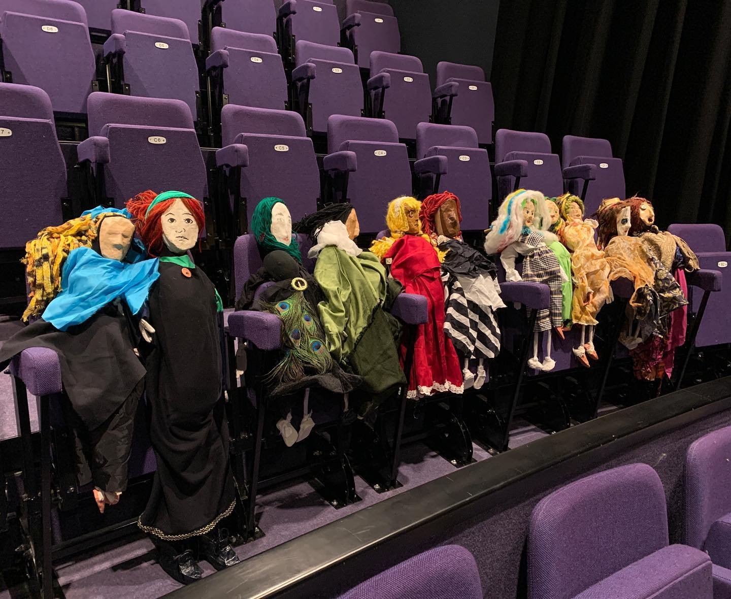 A row of handmade fabric puppets seated in theatre seats, made by Lockarts participants for a community performance.